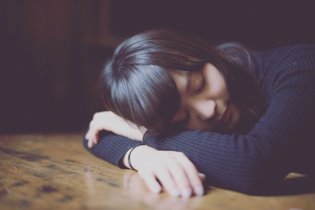 睡眠不足で机で寝てしまっている女性