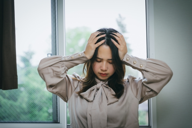 頭を抱えて悩む女性。ストレスが溜まっていると身体が緊張しやすく、楽器演奏のときには脱力しにくくなる。