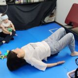 見守りスタッフがお子さんを抱っこしている横でストレッチポールでのエクササイズを行うママの様子